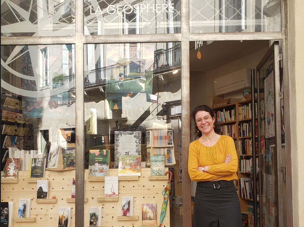 Magali, la gérante de la Librairie La Géosphère sur le pas de porte de la librairie