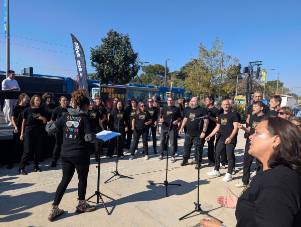 chorale Sunny Chorus en action devant rame de tramway micros sur pied ciel bleu arbre