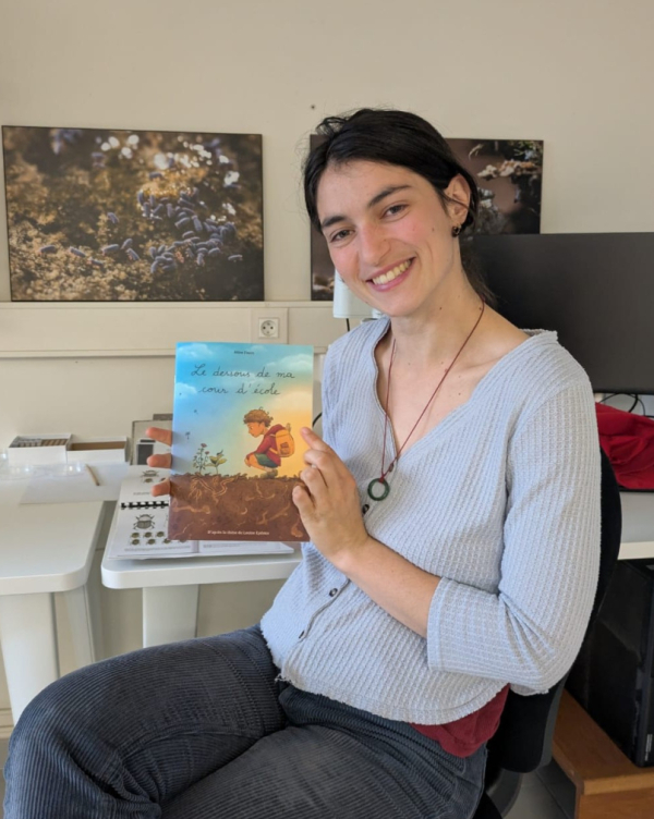 La post-doctorante Louise Eydoux pose avec la BD illustrant sa thèse, photos et ordinateur en arrière-plan